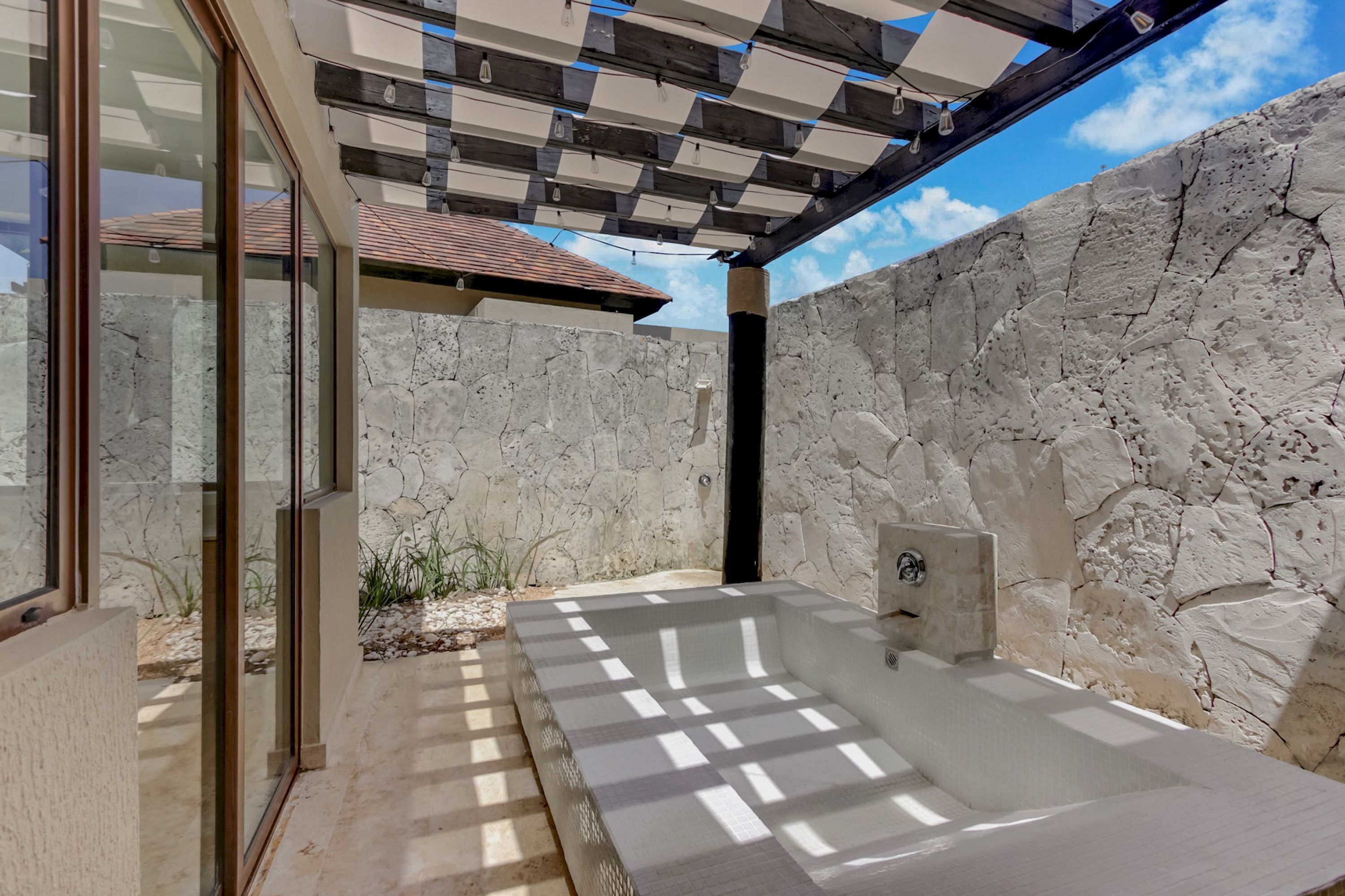 Une salle de bain extérieure moderne avec un mur en pierre, une porte en verre et une baignoire intégrée.