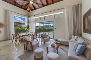 A spacious living room with a dining area, large windows, and a view of a swimming pool. - Luxury Cap Cana Villa With 3 Bedrooms Plunge Pool Maid and Golf Course Access (Punta Cana)