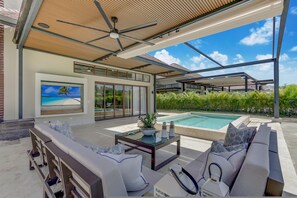 A modern outdoor living area with a pool, comfortable seating, and a ceiling fan.
