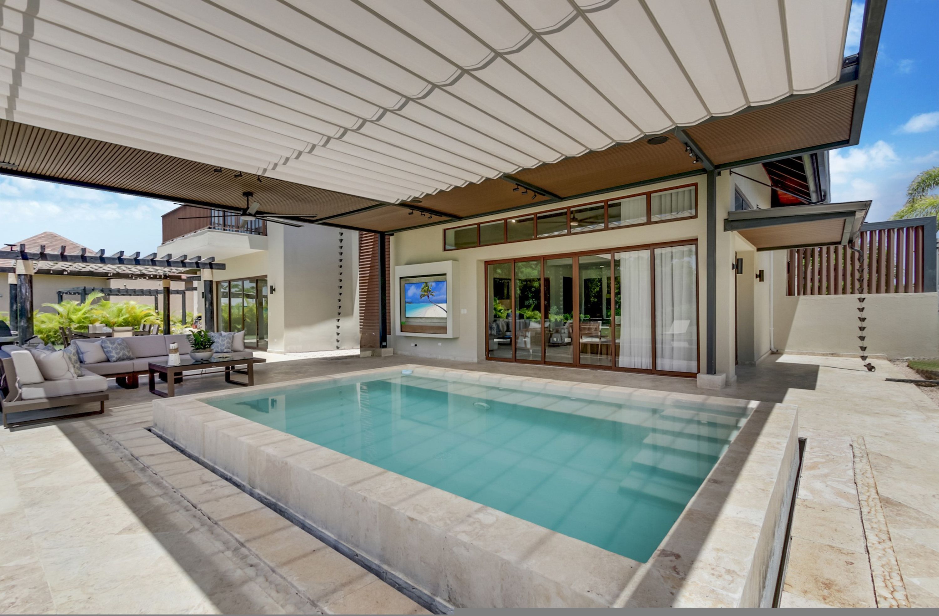 Ein moderner Poolbereich im Freien mit überdachter Terrasse, Sitzgelegenheiten und einem großen Fenster mit Blick auf den Pool.