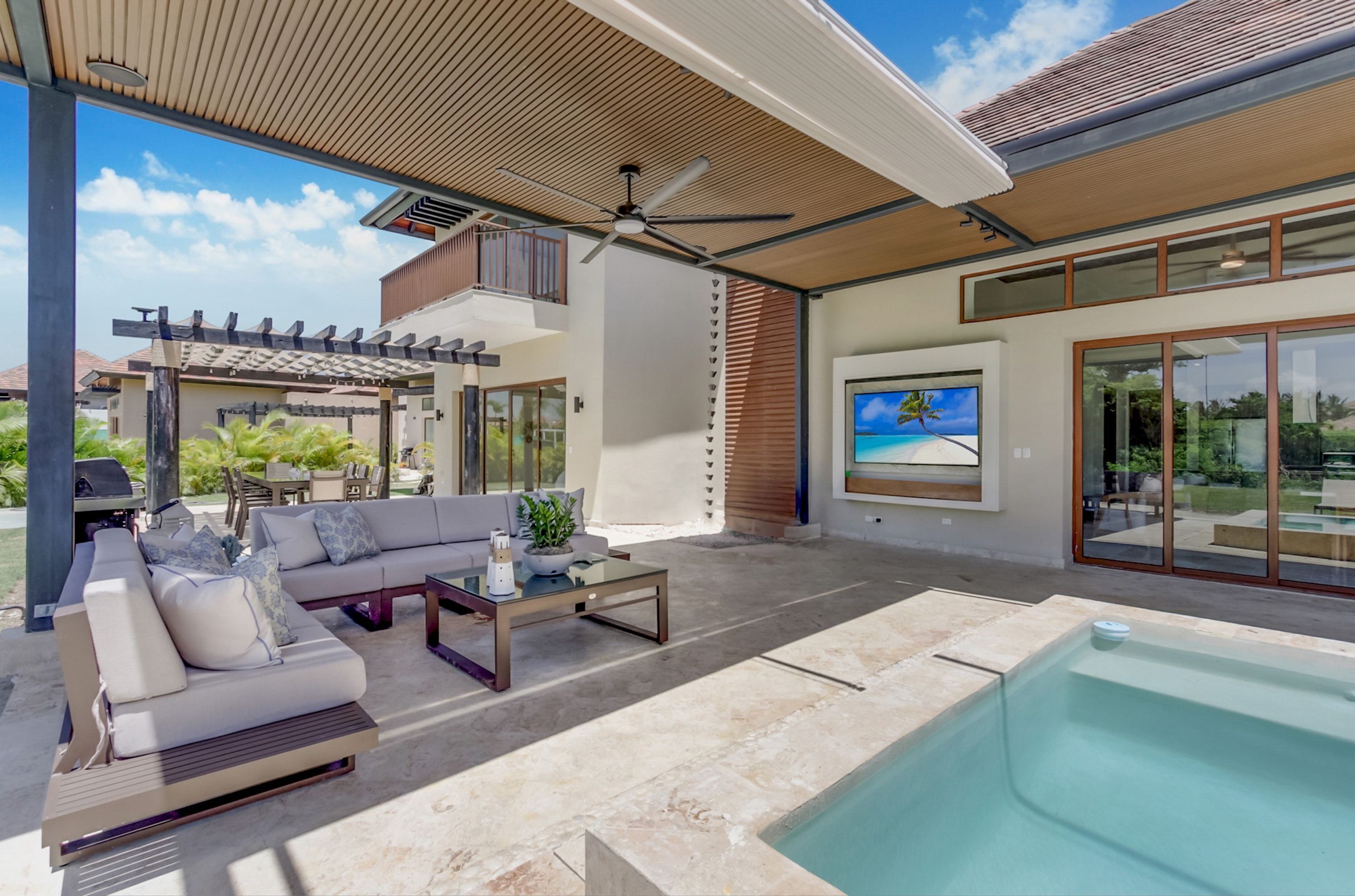 A modern outdoor living area with a pool, a sofa, and a ceiling fan.