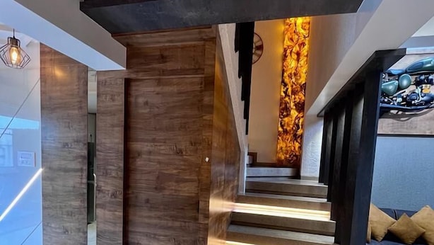 A modern staircase with wooden accents and integrated lighting, leading to a living area with a sofa and cushions. - Doves Mannat Villa  (Mawal)