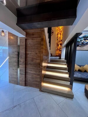 A modern staircase with wooden accents and integrated lighting, leading to a living area with a sofa and cushions. - Doves Mannat Villa  (Mawal)