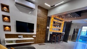 A modern living room with a grey sofa, a flat-screen TV, and a wooden accent wall. - Doves Mannat Villa  (Mawal)