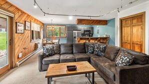 A modern living room with a sectional sofa, a wooden coffee table, and a kitchen area in the background.