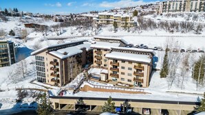 Un hotel a più piani con tetto innevato, un parcheggio sotterraneo e una stazione sciistica sullo sfondo.