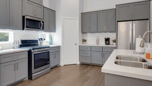 Une cuisine moderne avec des meubles gris, des appareils en acier inoxydable et un plan de travail blanc.