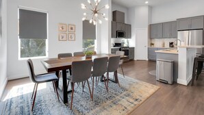 Une cuisine moderne avec des meubles gris, des appareils en acier inoxydable et un coin repas comprenant une table en bois et des chaises grises.