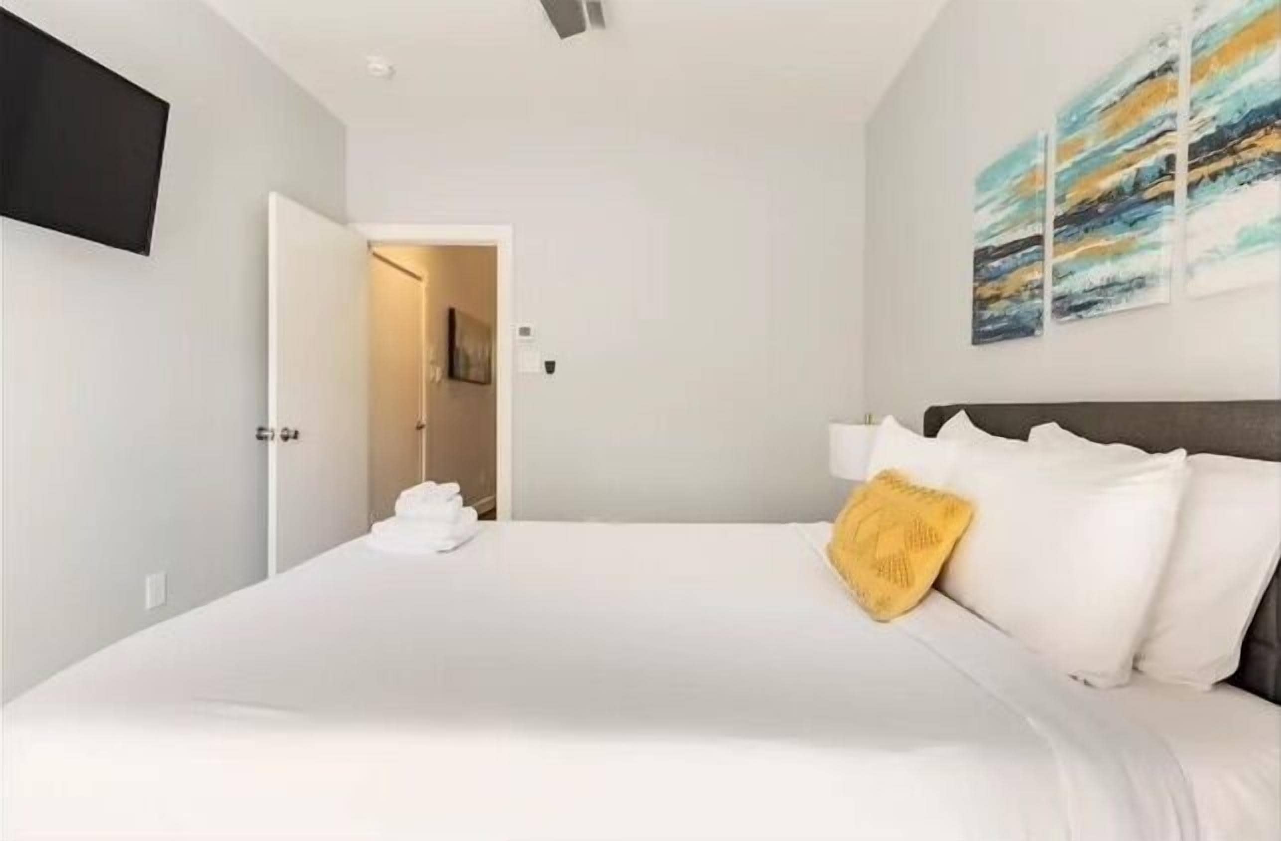 Ein modernes Hotelzimmer mit einem großen Bett, einem flachbildfernseher an der Wand und einem Gemälde über dem Bett.