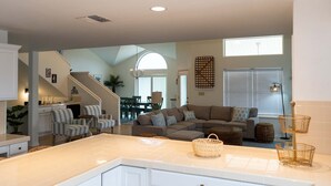 A spacious living area with a large sectional sofa, a kitchen with a white countertop, and a dining area with a table and chairs.