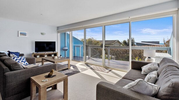 A modern living room with a large sliding glass door leading to a deck, a flat-screen TV, and a cozy seating area. - Osbourne walk to beach (Cowes)