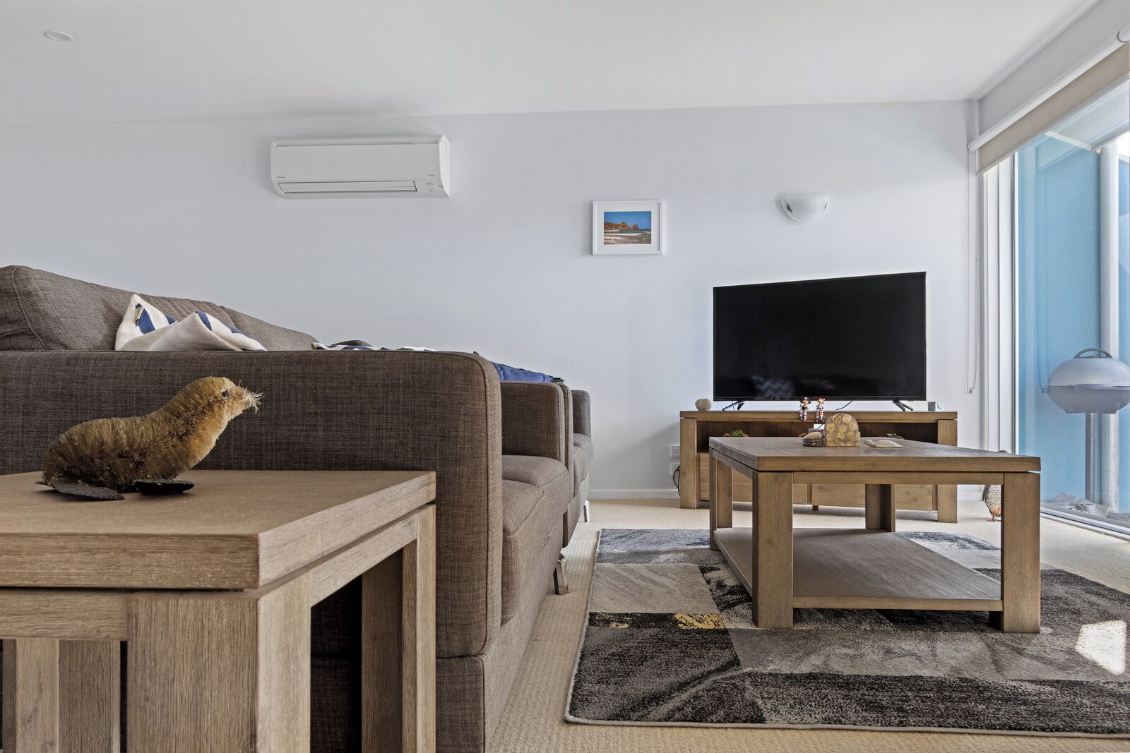 A modern living room with a sofa, a coffee table, a television, and a small table with a decorative item.