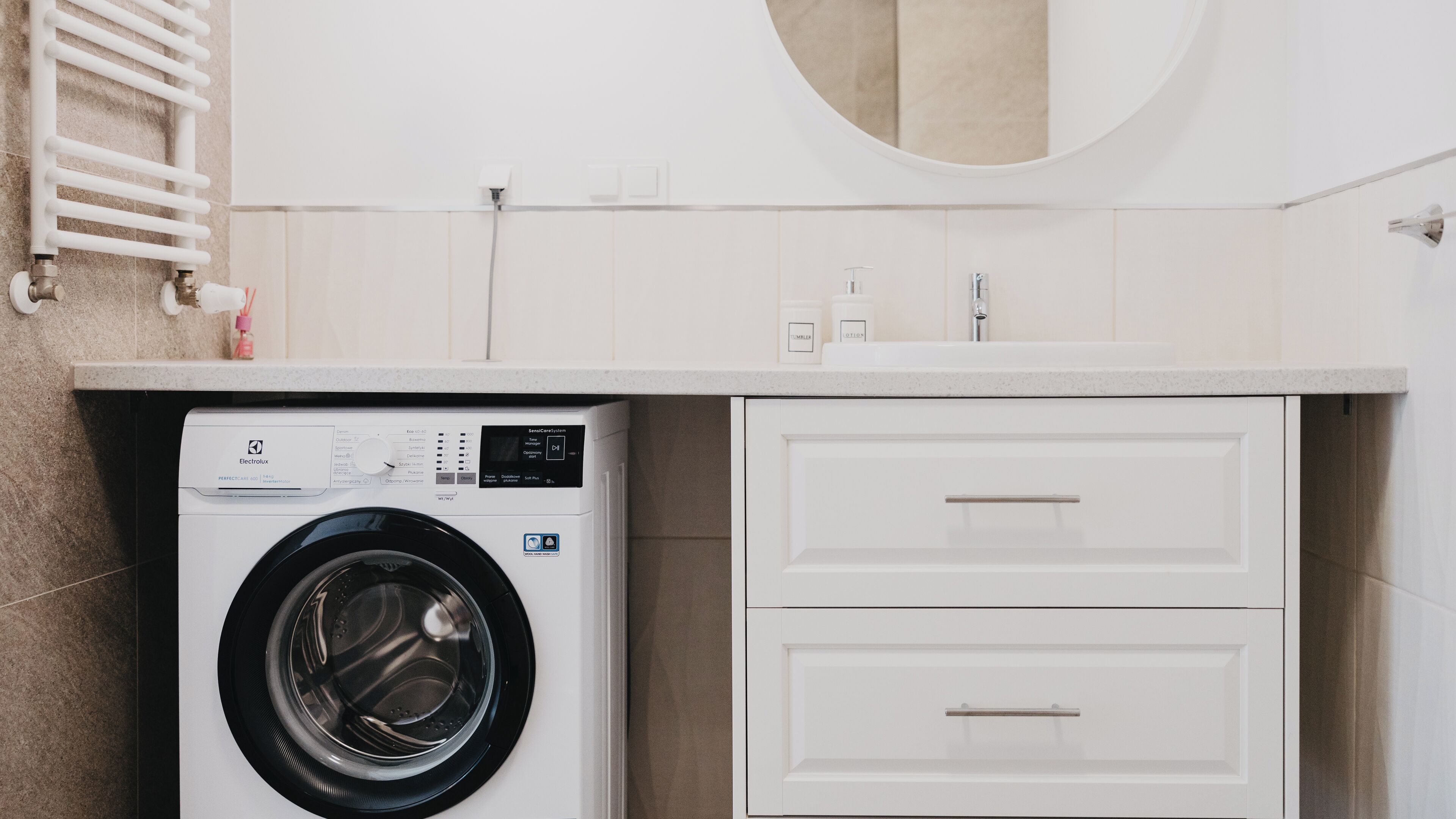 A compact laundry area with a front-loading washing machine, a countertop with a sink, and a mirror above the countertop.