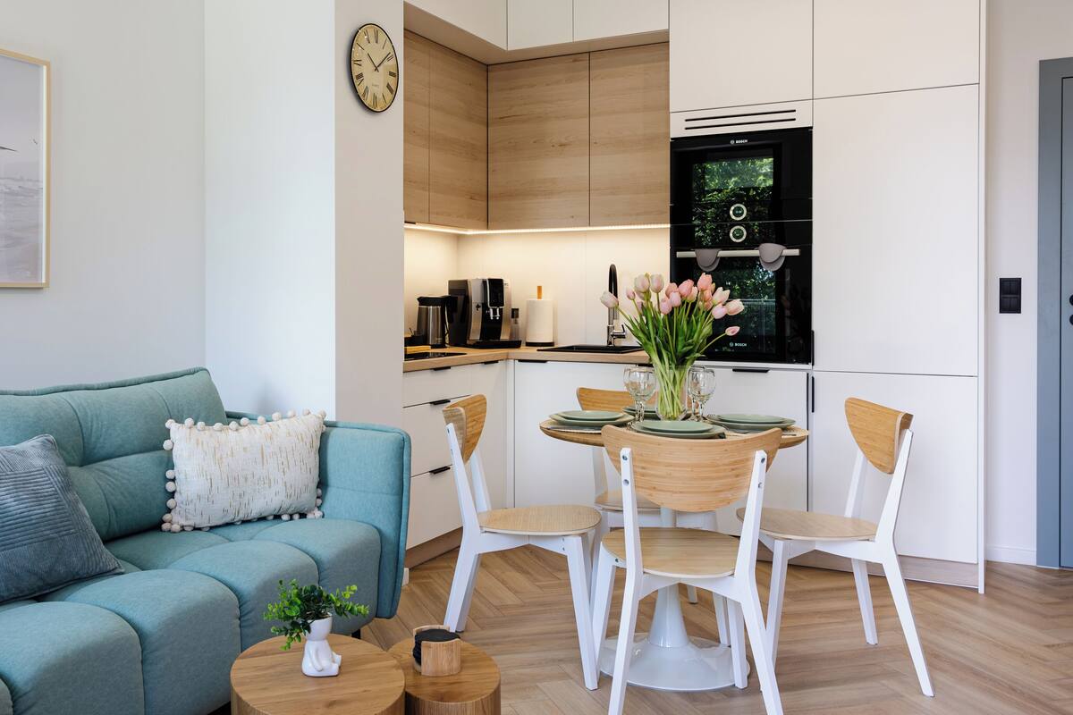 A modern living room with a teal sofa, a coffee table, and a dining area with a wooden table and chairs.