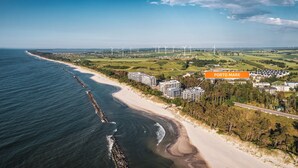 Eine Vogelperspektive auf Porto Mare mit Strand, Windkraftanlagen und Wohnhäusern.