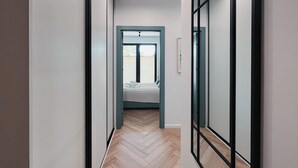 Ein schmales Treppenhaus mit Holzdielen im Fischgrätmuster, das zu einem Schlafzimmer mit Bett und Fenster führt.