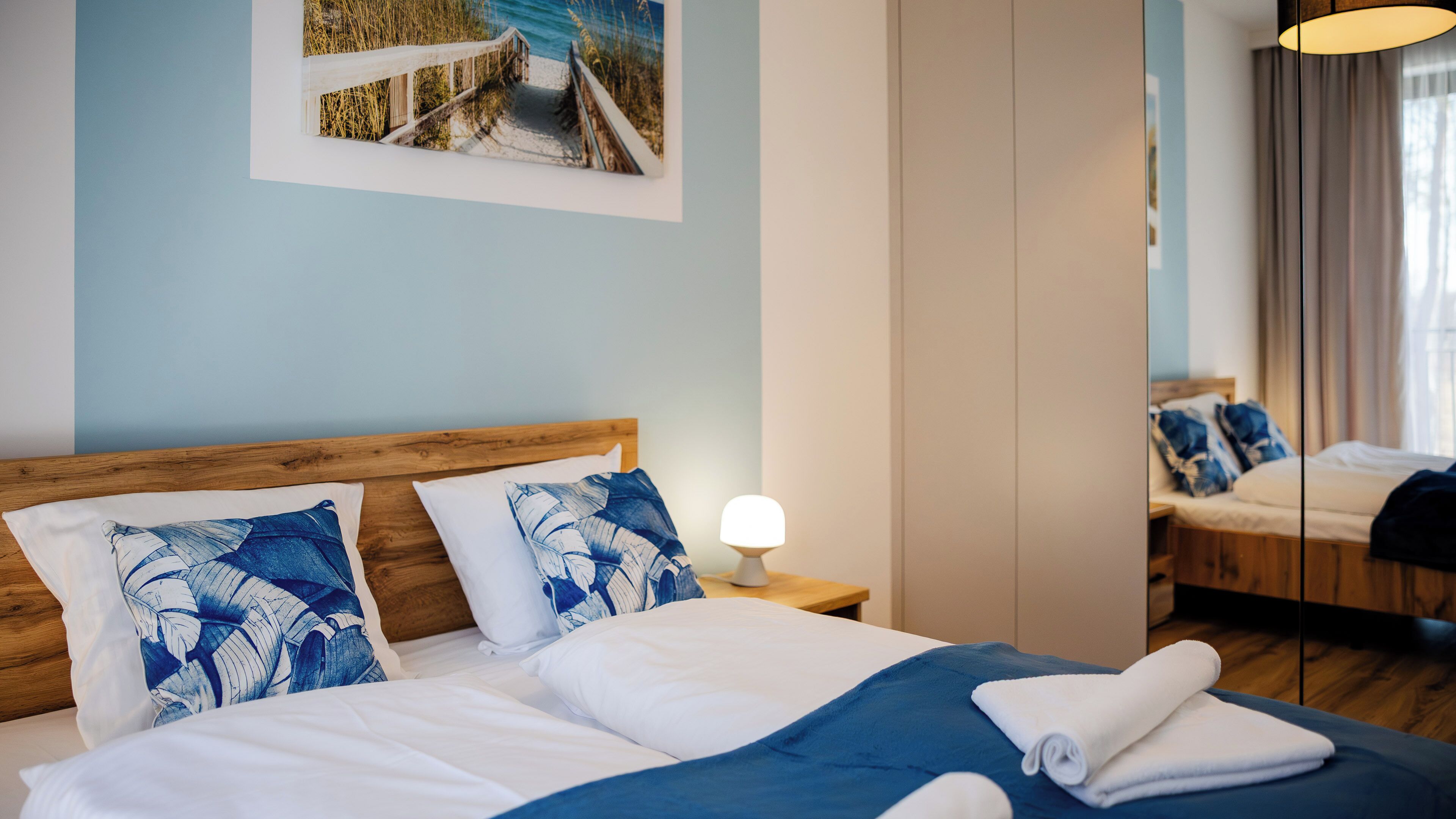 Ein Hotelzimmer mit Bett, Kissen, Nachttisch, Lampe, Spiegel und einem Bild an der Wand.