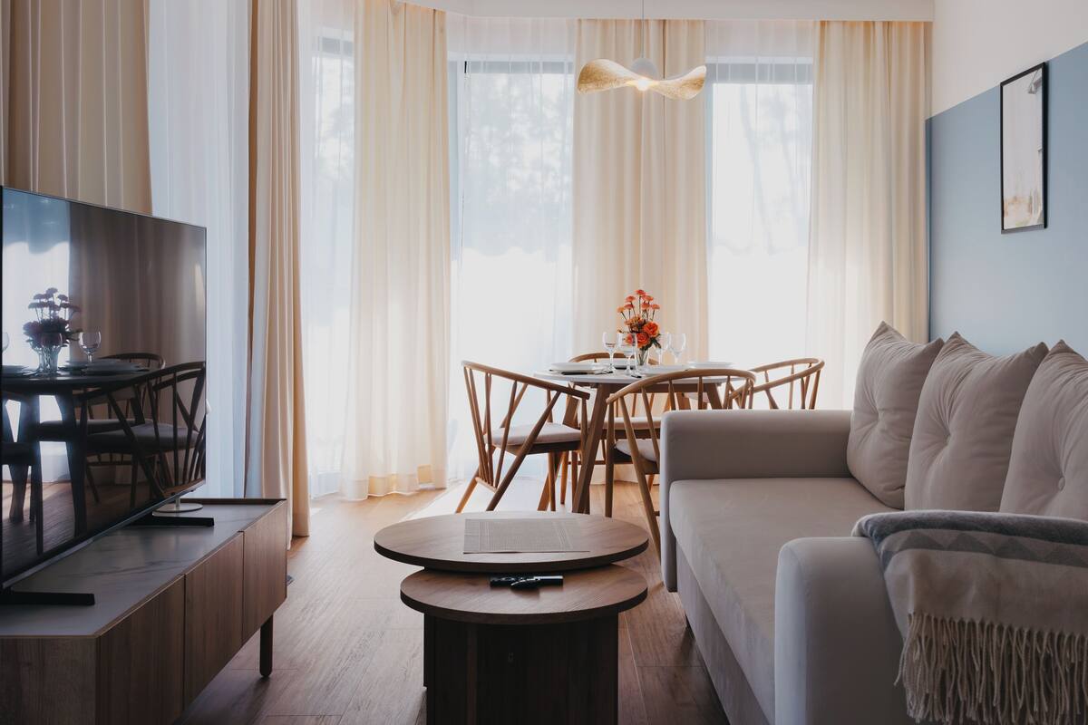 A modern living room with a sofa, a dining table with chairs, a TV, and a small round table.