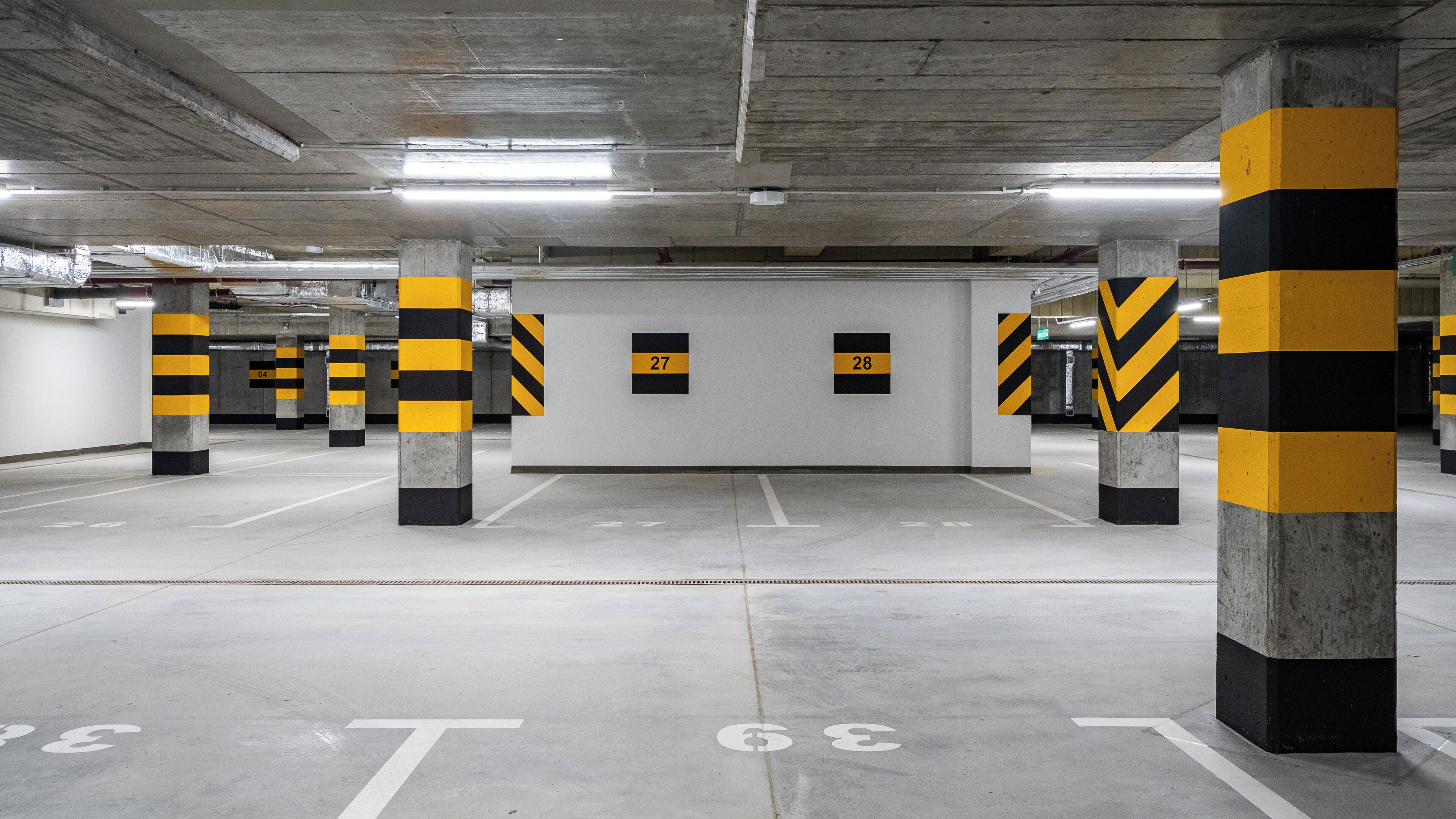 Een parkeergarage met betonnen pilaren, witte muren en genummerde parkeerplaatsen.