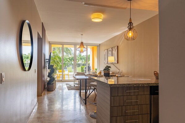 A modern kitchen with a built-in dishwasher, a dining area with a table and chairs, and a large window offering a view of palm trees.