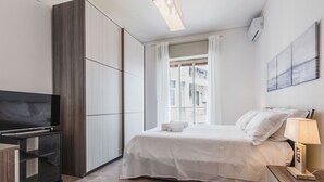 A modern hotel room with a bed, a TV, a bedside table, and a window with curtains. - Casa Adda by Wonderful Italy - Plutone (Syracuse)