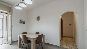 A dining area with a wooden table and chairs, a clock on the wall, and a hallway leading to another room. - Casa Adda by Wonderful Italy - Plutone (Syracuse)