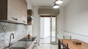 A modern kitchen with a sink, stove, and wooden cabinets. There is a dining table with chairs and a view of the outside through a glass door. - Casa Adda by Wonderful Italy - Marte (Syracuse)