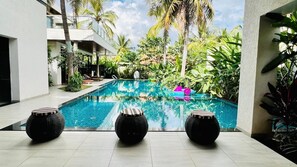A swimming pool with three round black stools in the foreground, surrounded by lush greenery and palm trees. - Narayani Revtree - Resort & Villa (Hospet)