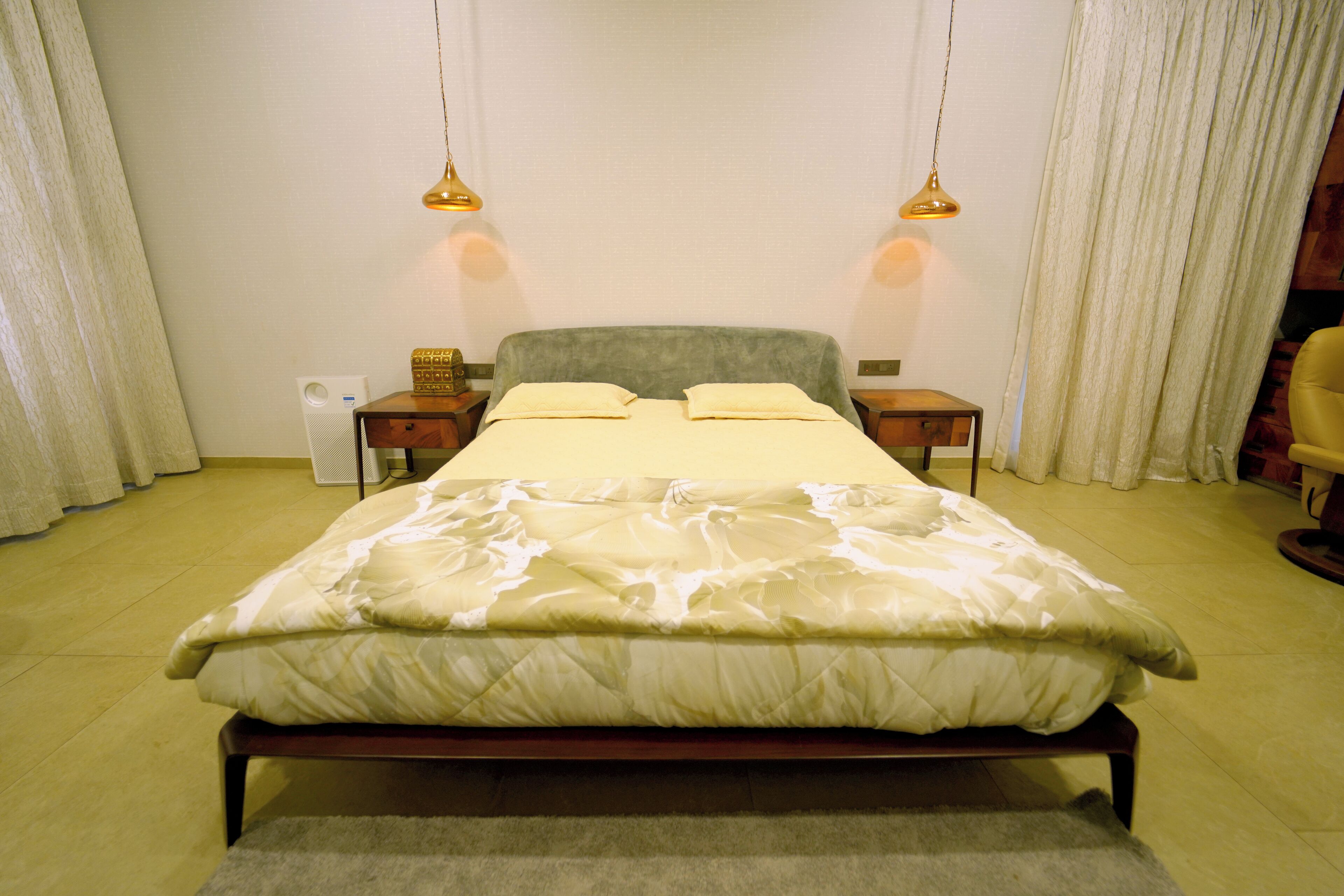 A neatly made bed with a green headboard, two bedside tables with lamps, and a white wall with a curtain.