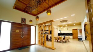 A spacious living area with a wooden ceiling, a dining area with chairs and a table, and a kitchen area with cabinets and a countertop. - Narayani Revtree - Resort & Villa (Hospet)