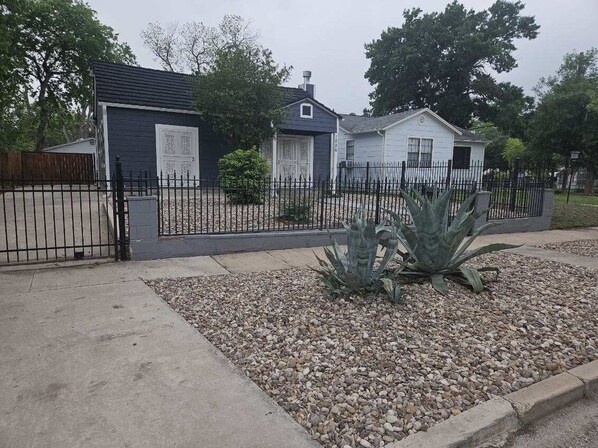 Een woonwijk met een omheind erf, een kleine schuur en een huis met een donkere gevel en een witte deur.