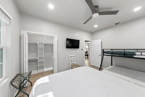 Een slaapkamer met een bed, een plafondventilator, een televisie, een kledingkast en een bureau met stoel.