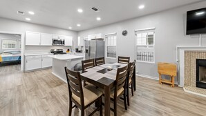 A modern kitchen with white cabinets, a central island, and a dining area with wooden chairs.