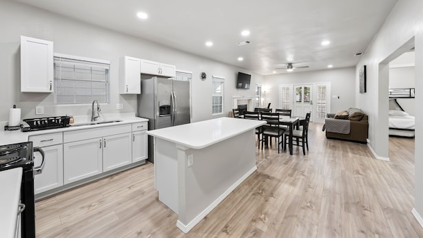 A modern kitchen with white cabinetry, a central island, and a dining area with a table and chairs.