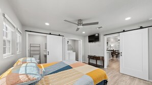 A bedroom with a bed, a ceiling fan, a TV, and a desk.
