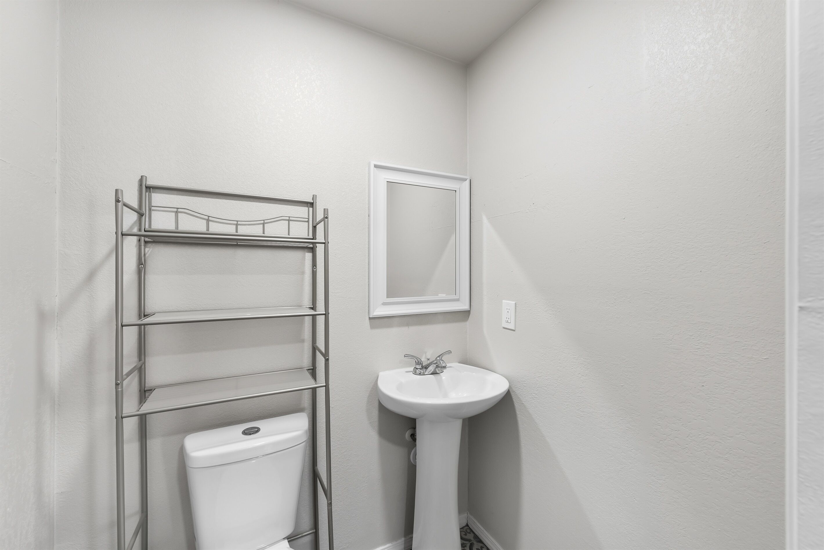 Une petite salle de bain comprenant des toilettes, une étagère en métal et un lavabo sur colonne.