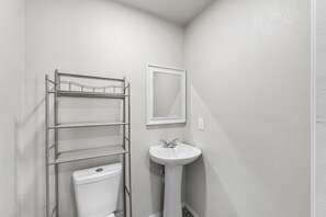 Een kleine badkamer met toilet, een metalen open kast en een wastafel op voet.