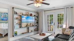 A living room with a large TV, a ceiling fan, a sofa, and a coffee table. - Walk to Beach: 7BR House w/ Private Pool & Hot Tub (Surfside Beach)