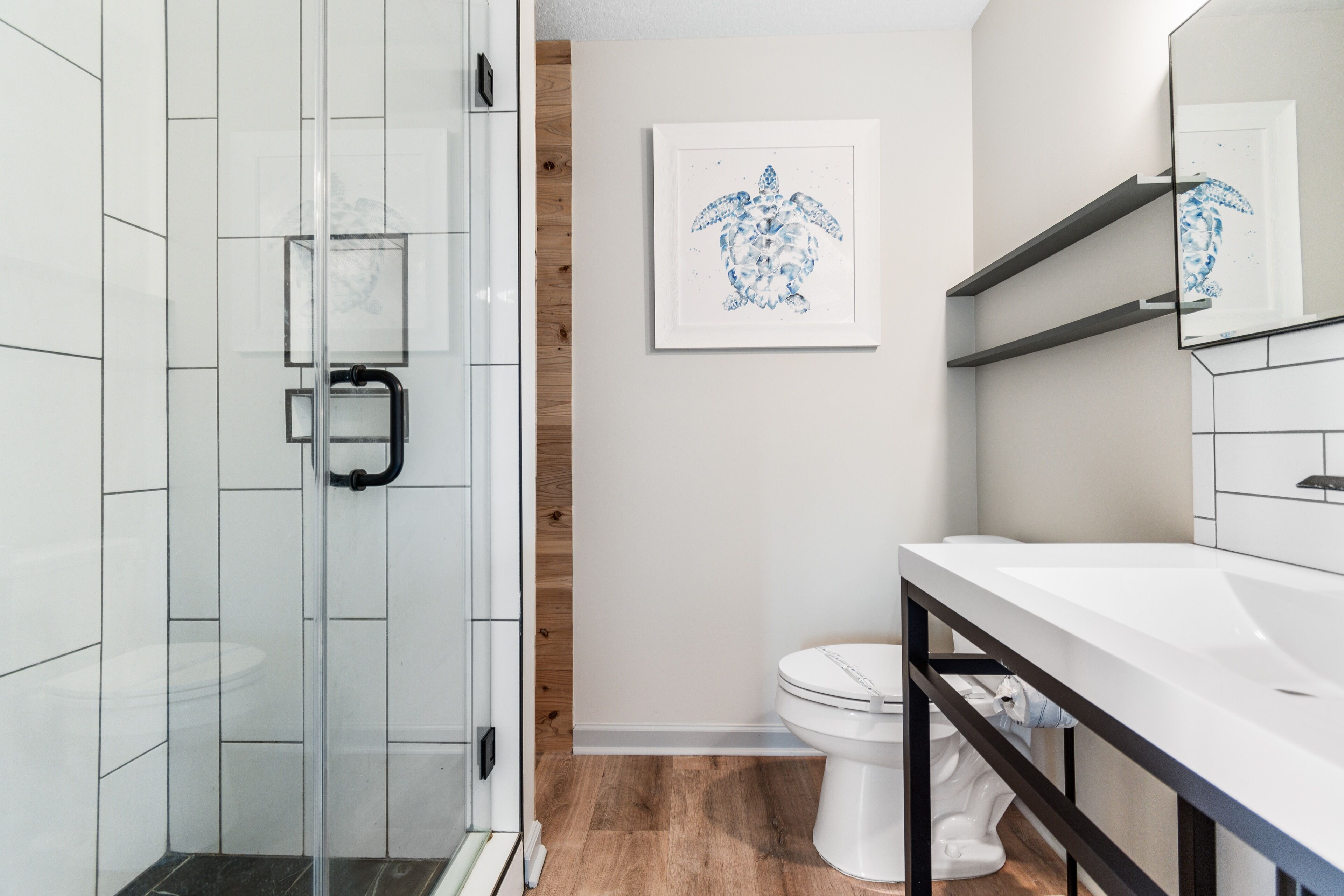 A modern bathroom with a glass shower enclosure, a white toilet, and a framed artwork on the wall.