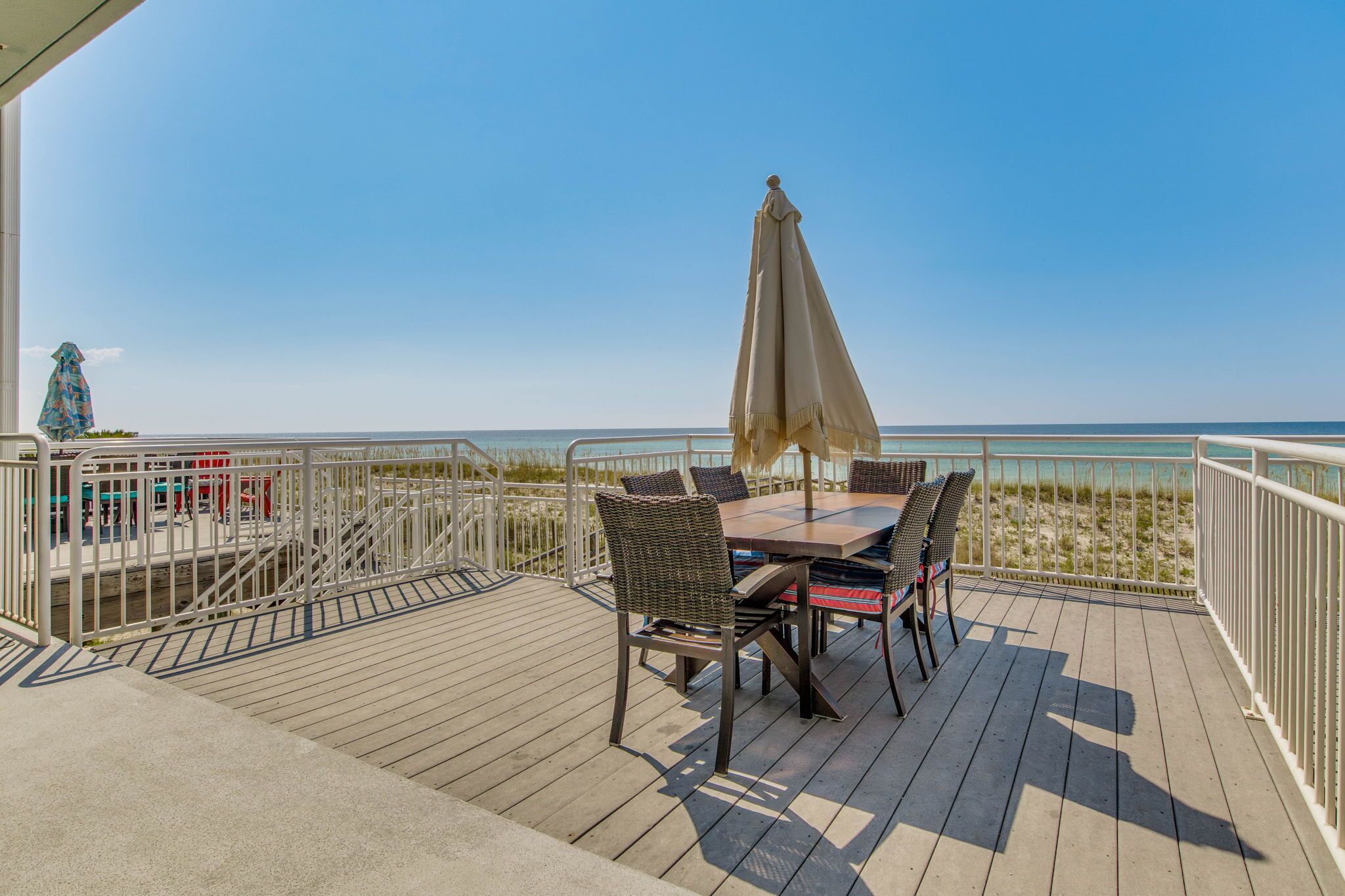 A deck with a table and chairs, overlooking a beach.