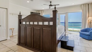Un dormitorio con una cama grande, ventilador de techo y balcón con vista al océano.