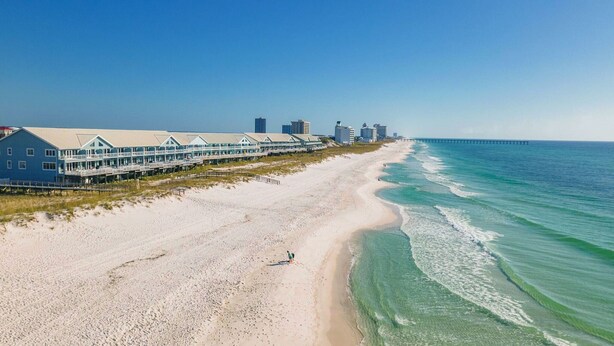 Un hotel frente a la playa con un edificio extenso que se extiende a lo largo de la orilla, un muelle y una vista despejada del océano.