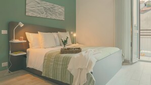 Et soveværelse med en seng, sengeborde, en lampe, et kunstværk på væggen og udsigt gennem en åben dør.