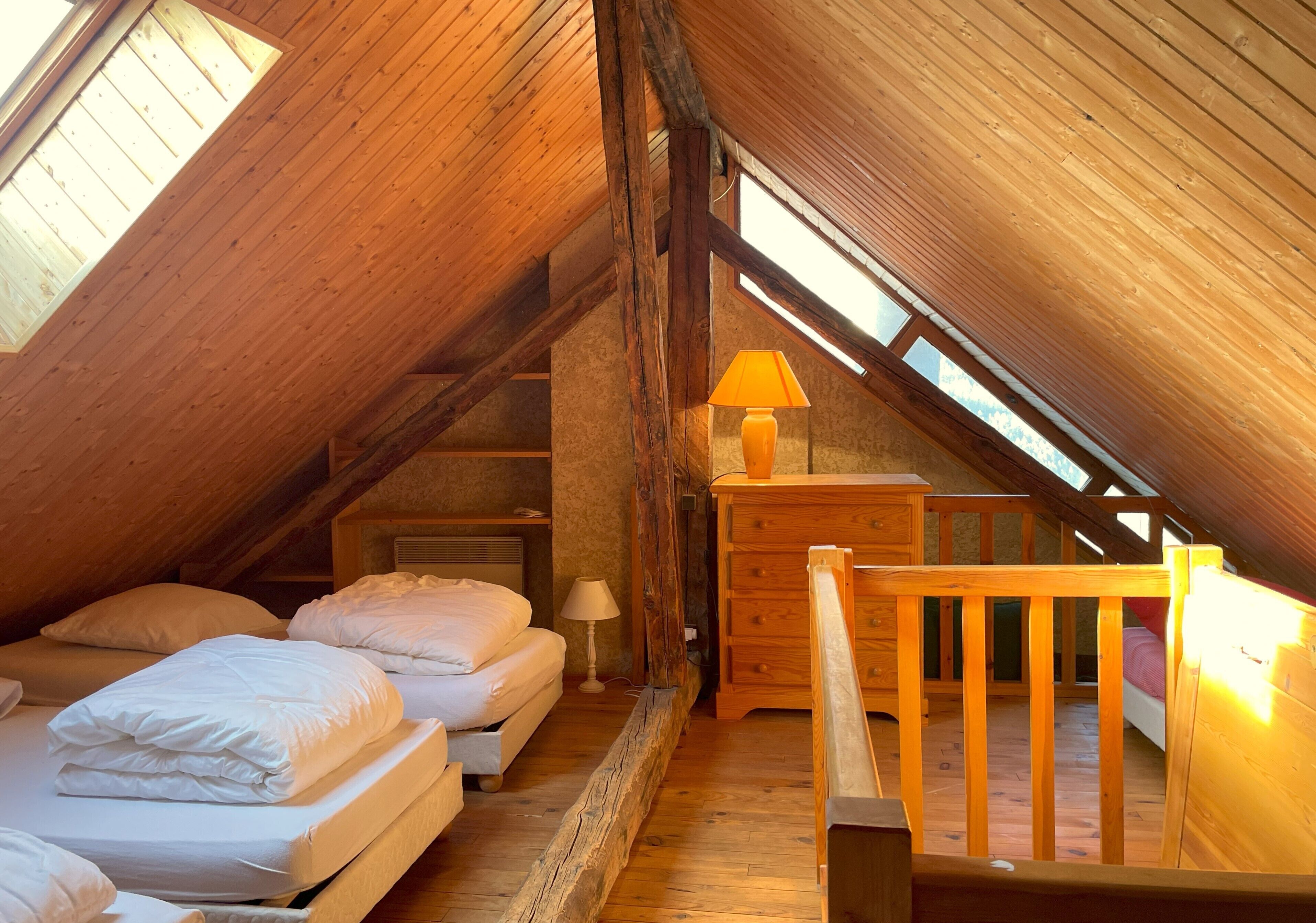 Quarto de sótão acolhedor com vigas de madeira, um aparador de madeira e uma cama com lençóis brancos.