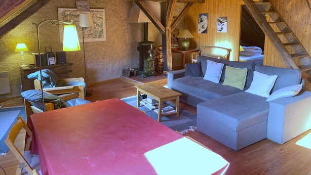 A cozy attic room with a wooden ceiling, a sofa, a table, and a lamp. - Flat in a country house.  
 (Saint-Chaffrey)