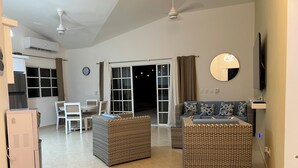 A living room with a sofa, two armchairs, a dining table with chairs, a TV, and a ceiling fan.