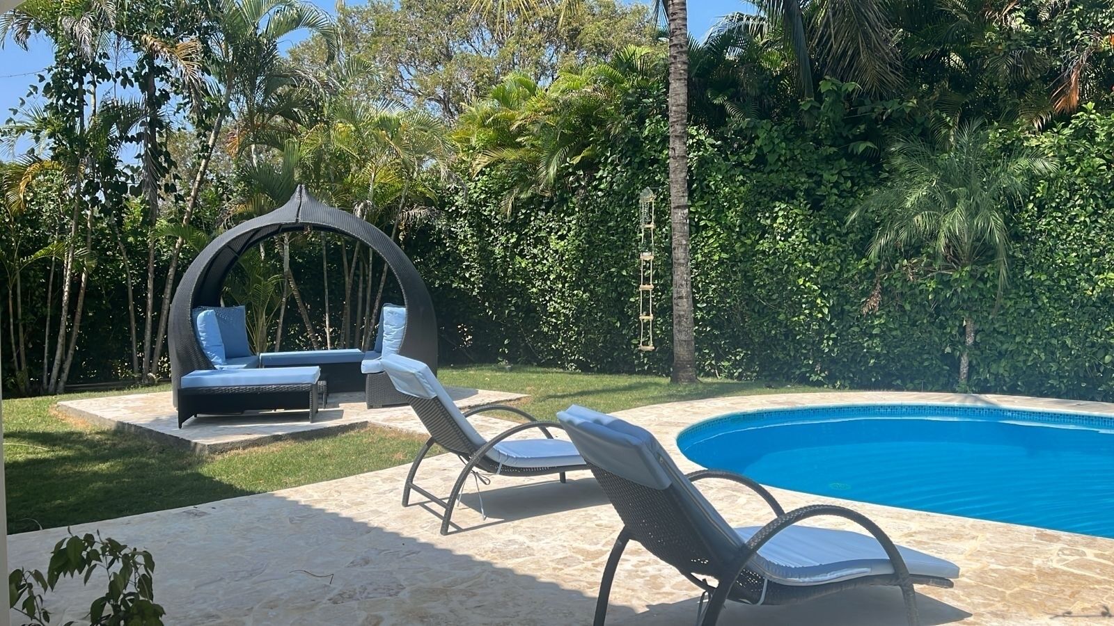 Zona junto a la piscina con sillones de descanso, una silla colgante y un pequeño rincón de estar con cojines.