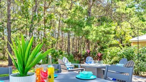An outdoor dining area with a table set for two, surrounded by chairs, a potted plant, and a glass of iced tea with fruit.
