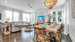 A spacious dining area with a wooden table and chairs, a chandelier, and a television on the wall.