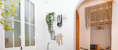 A compact kitchen with a sink, stove, and a small countertop. There are plants and kitchen utensils on the wall.